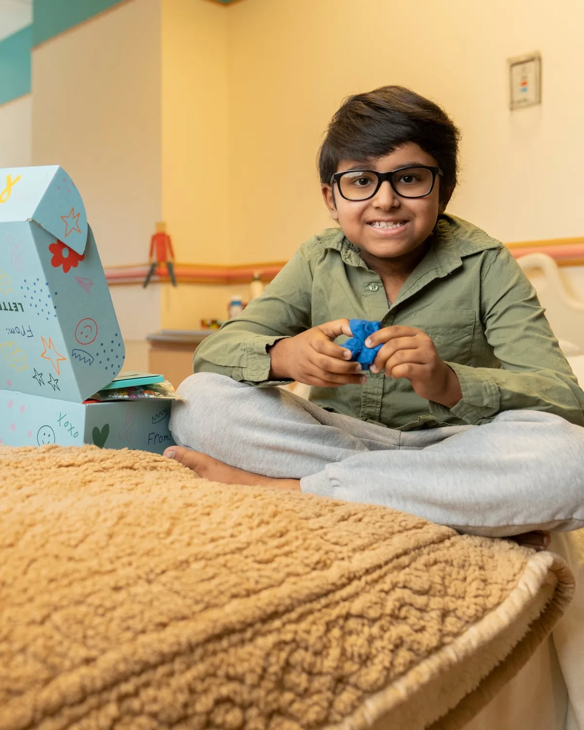 Smiling boy sitting cross-legged on his hospital bed next to his open Boombox